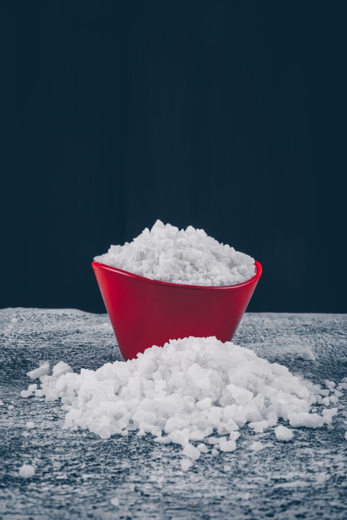 sea salt in a red bowl and around on a dark textured and black background. side view.