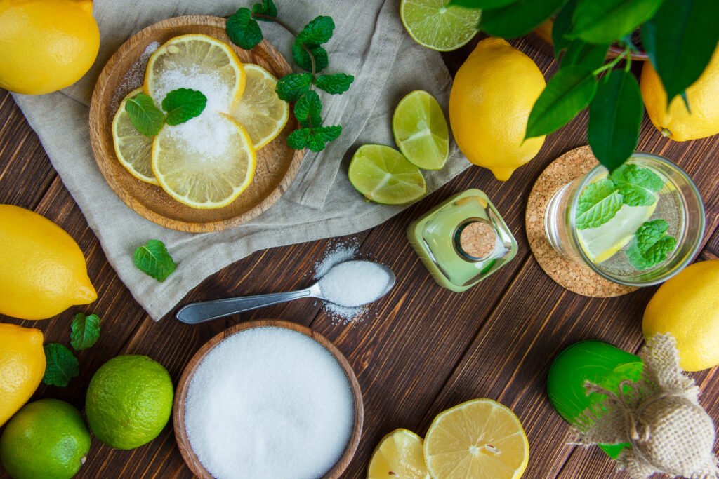 lemons in a plate with drinks, salt, herbs, limes flat lay on wooden and kitchen towel background